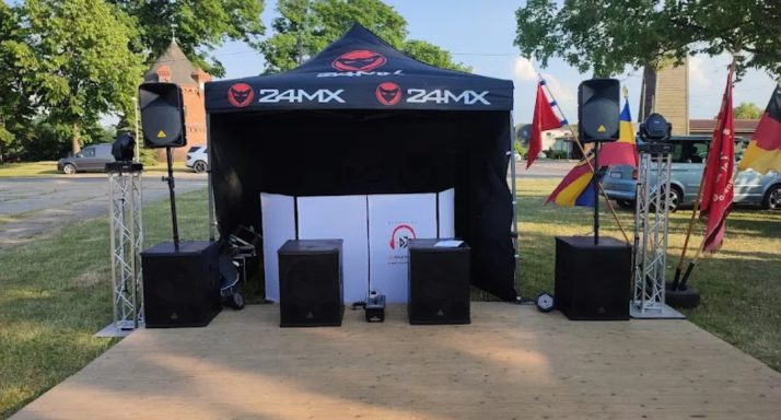 Zelt mit Lautsprechern und Flaggen auf einem Rasenplatz, Bühne vorbereitet für eine Veranstaltung.